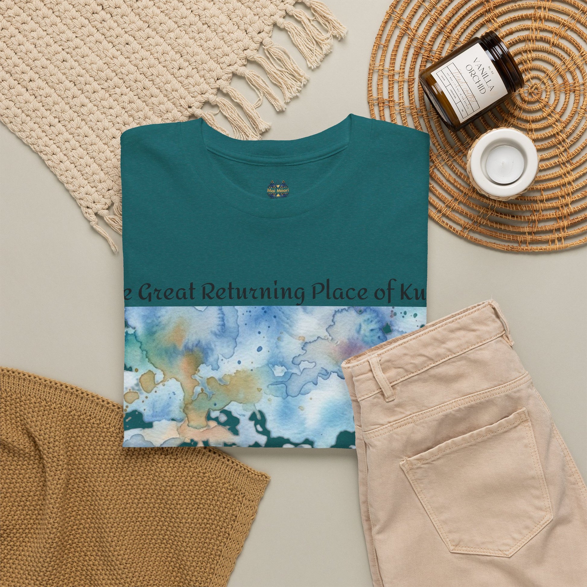 Teal graphic T-shirt folded with crew neck and watercolor landscape print on front.