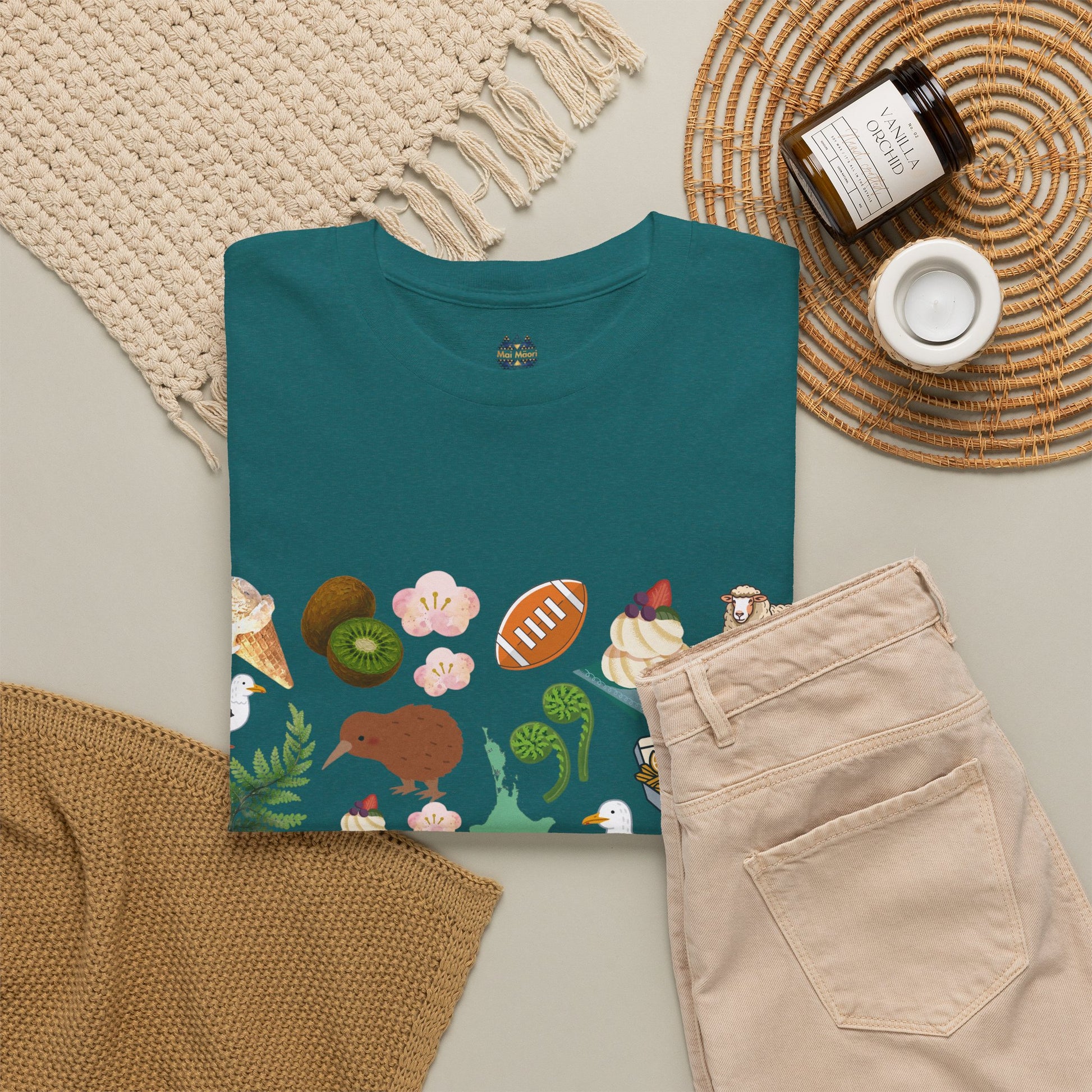 Teal crewneck T-shirt with Kiwiana-themed print hem; shown folded with jeans nearby