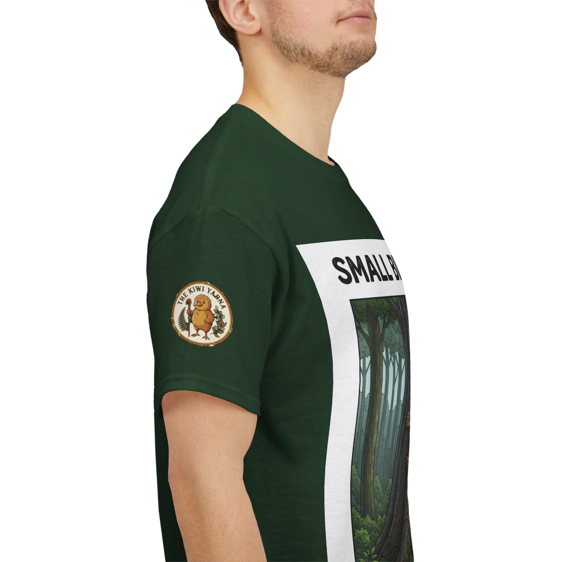 Dark green T-shirt side view with sleeve patch and “SMALL BIRD” text over forest