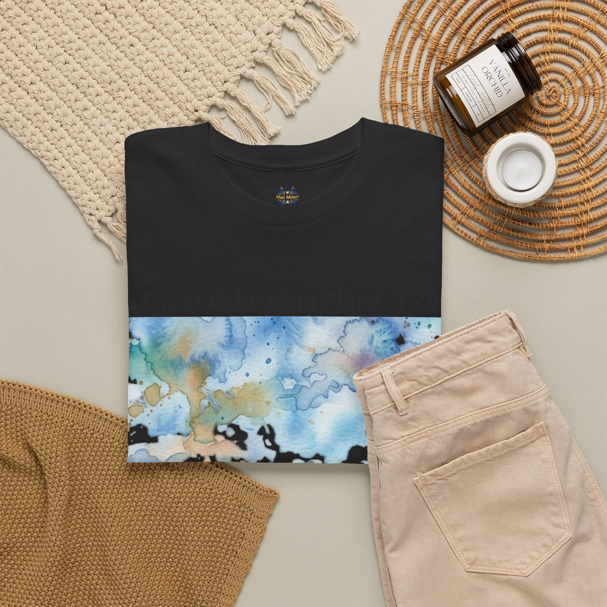 Black graphic T-shirt folded with watercolor landscape artwork and small chest logo