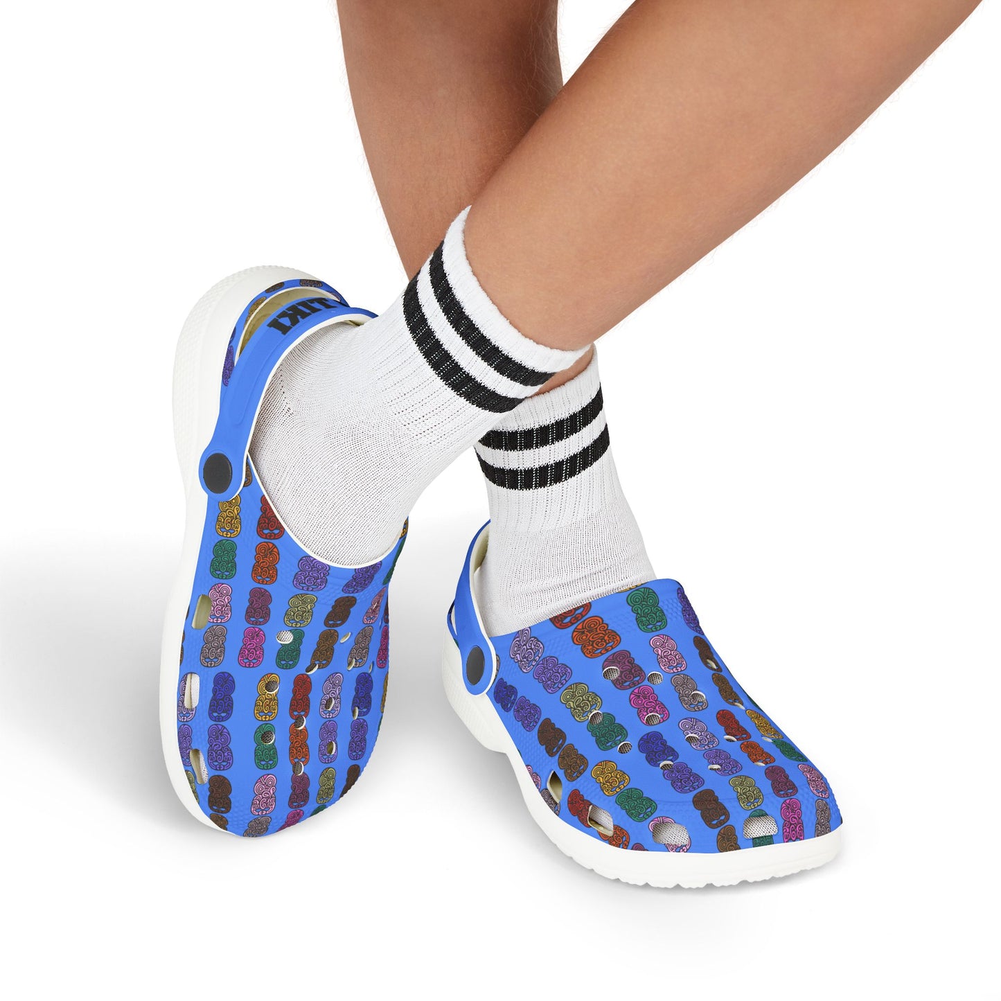 Kids slip-on casual shoe with multicolor tiki-print upper, white sole, worn with striped socks