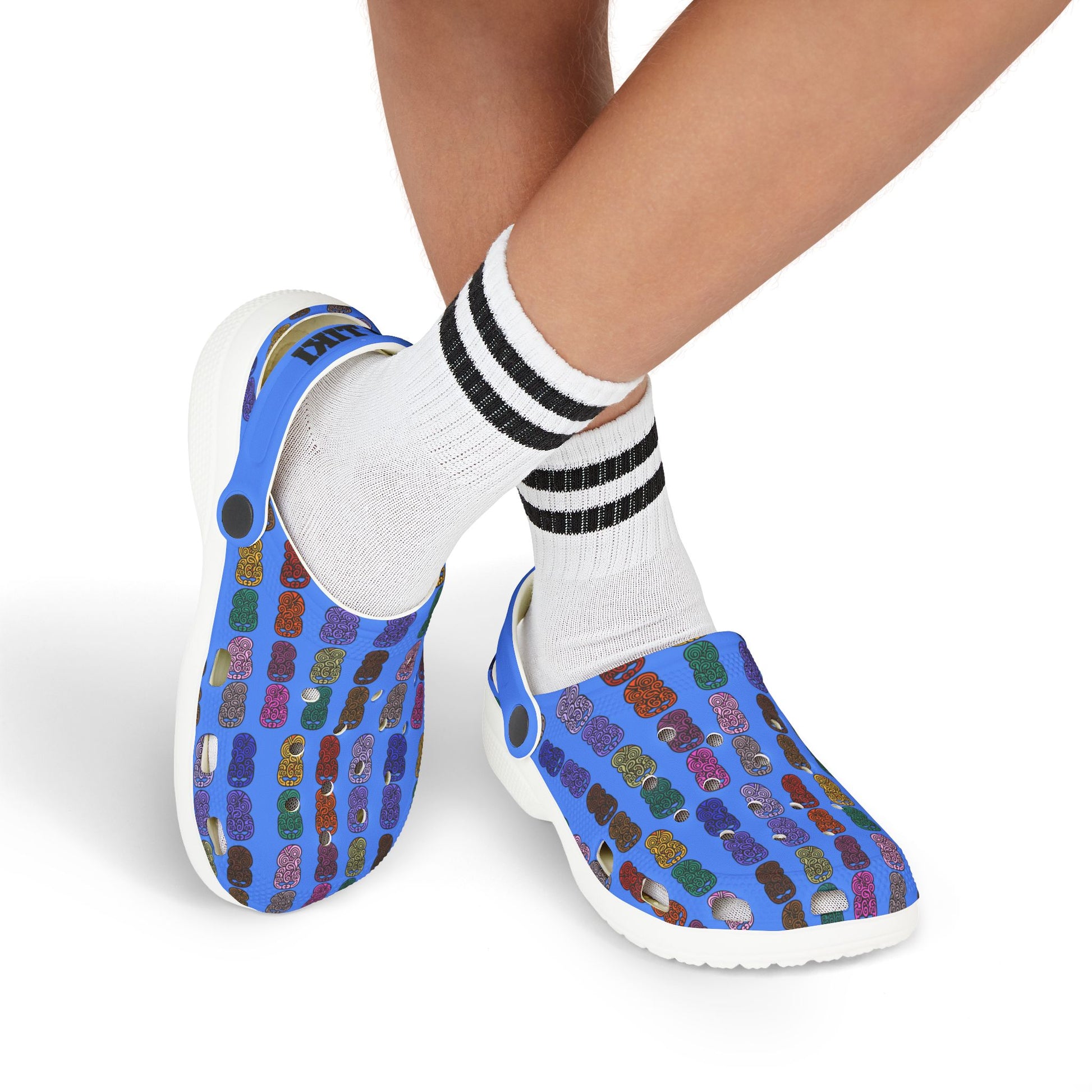 Kids slip-on casual shoe with multicolor tiki-print upper, white sole, worn with striped socks